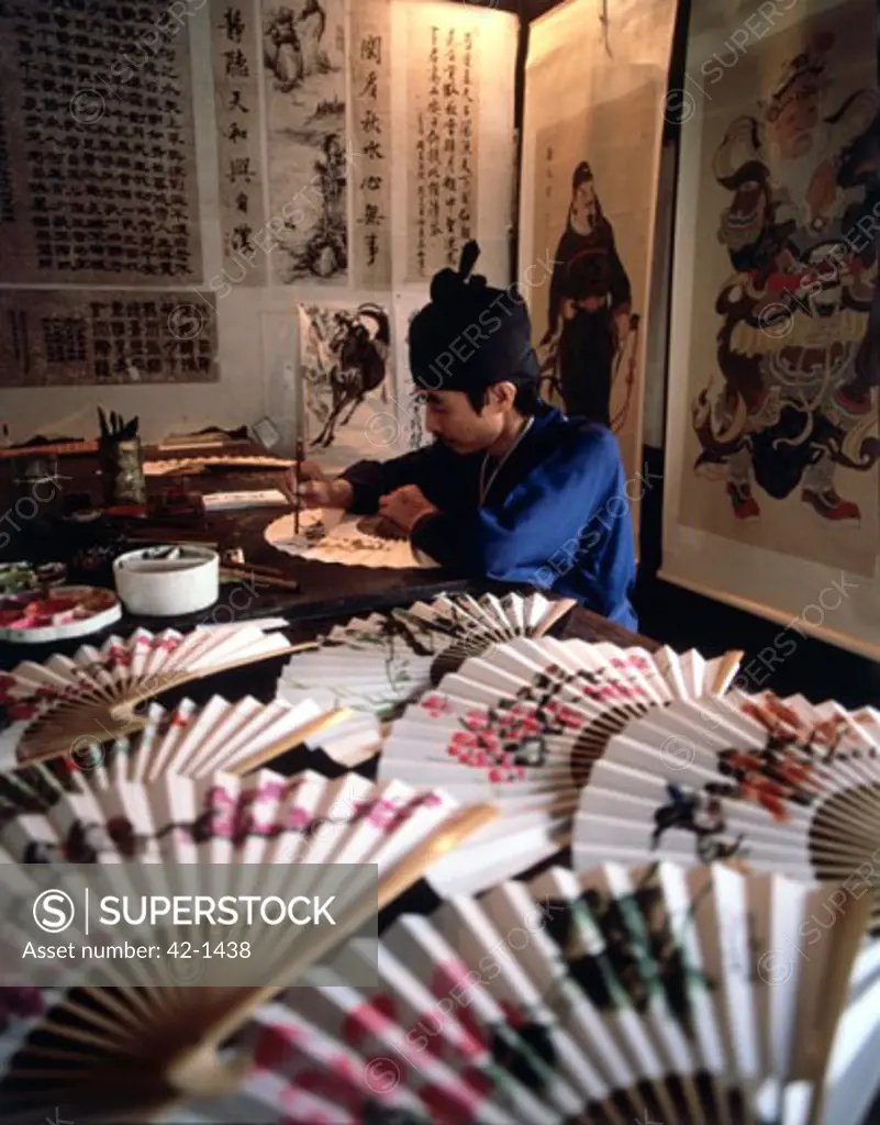Side profile of a mid adult man painting on a folding fan, Hong Kong, China