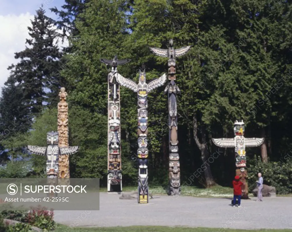 Two tourists standing in front of a totem pole, Stanley Park, Vancouver, British Columbia, Canada