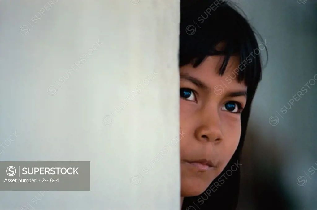 Close-up of a girl peeping from behind a wall