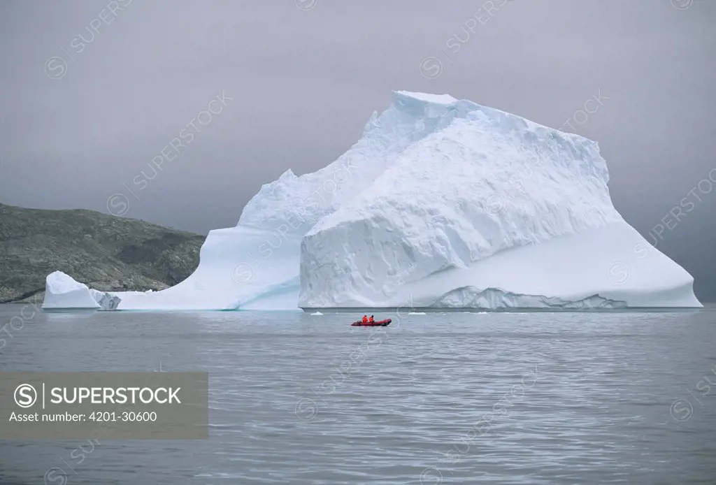 Red rubber boat with two expedition members circle floating iceberg, summer season, Labrador Sea, Labrador, Canada