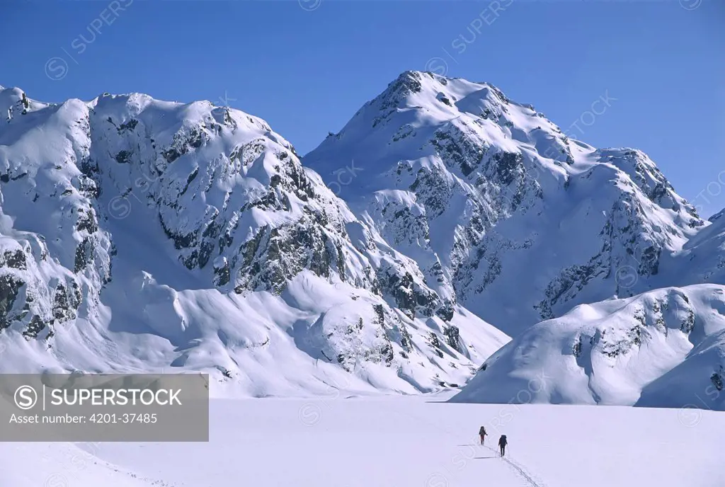 Skiers cross frozen surface of Lake Harris along the Routeburn Track in winter, Mt Aspiring National Park, New Zealand