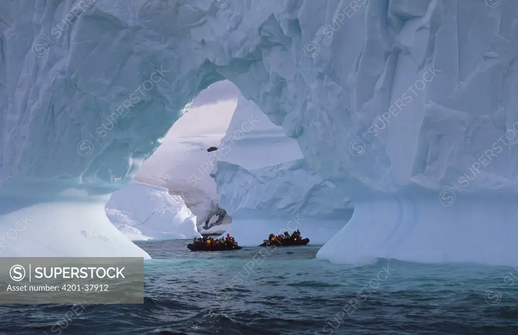 Tourists cruise in inflatable boats, close to large iceberg arch, Enterprise Island, Antarctica Peninsula, Antarctica