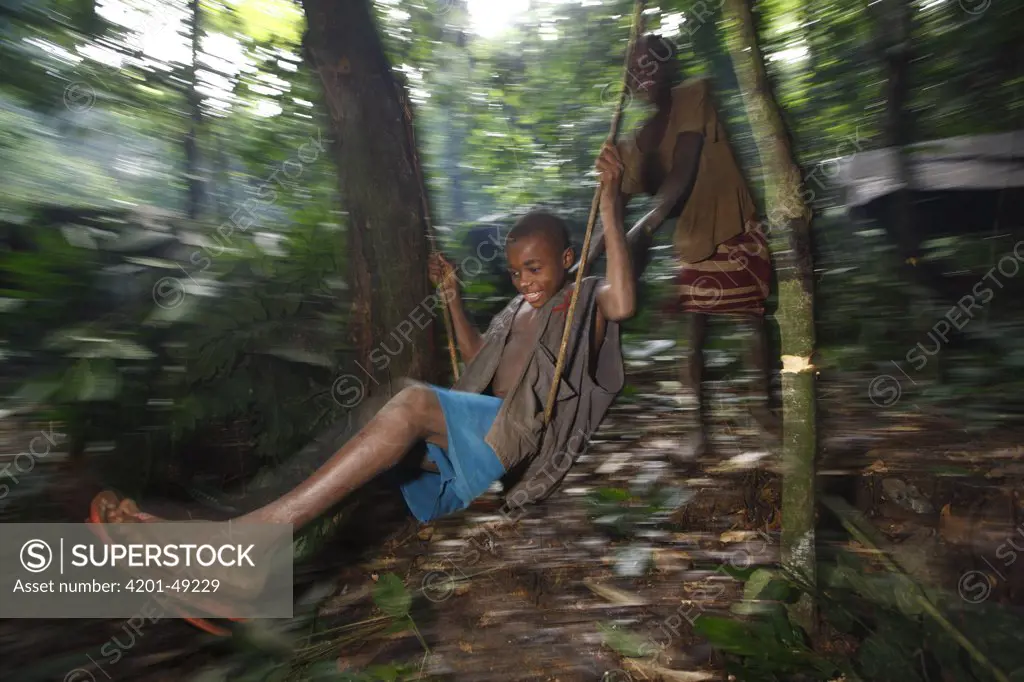 Baka child swinging on liana in the forest, Cameroon