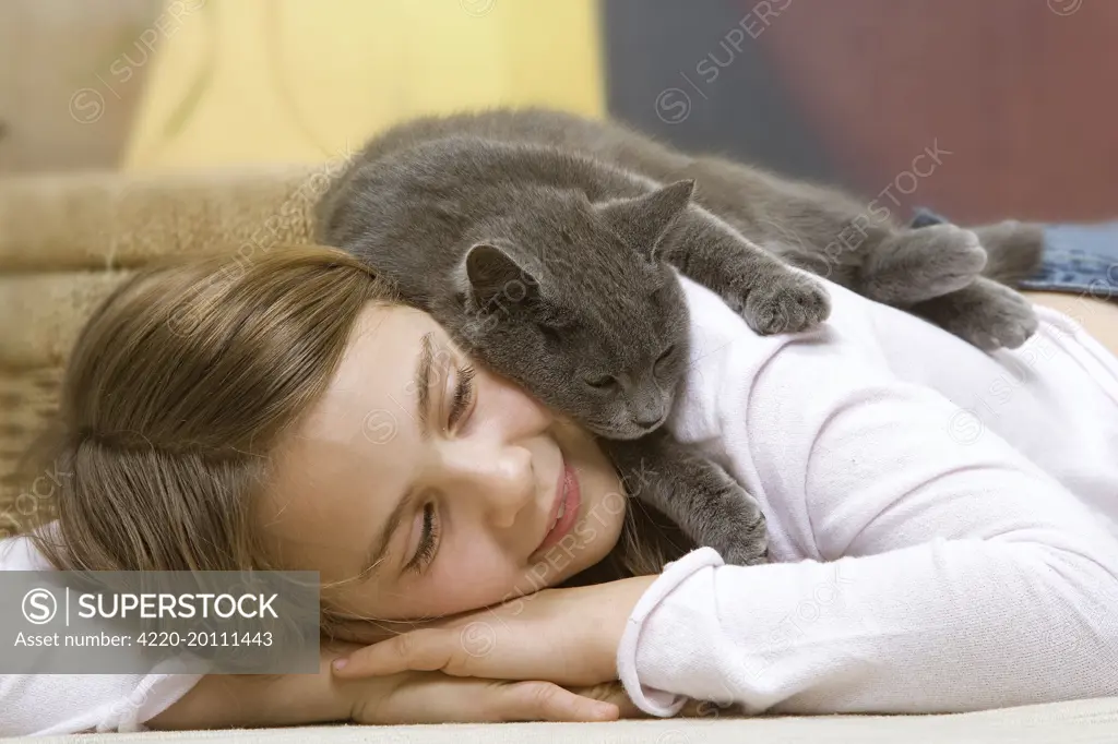 Cat - Young girl lying on floor with grey cat sleeping on her back. 