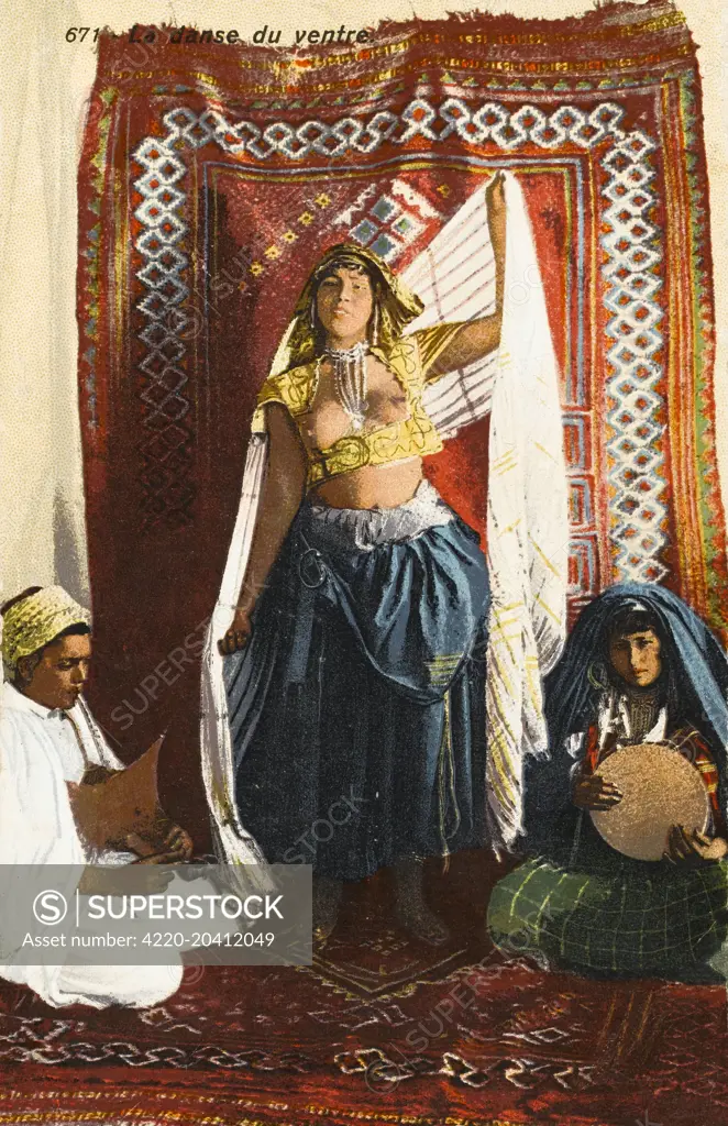 Algerian bellydancer in very revealing and exotic garb, performing on a fine rug, with two seated musicians to each side.     Date: circa 1910s
