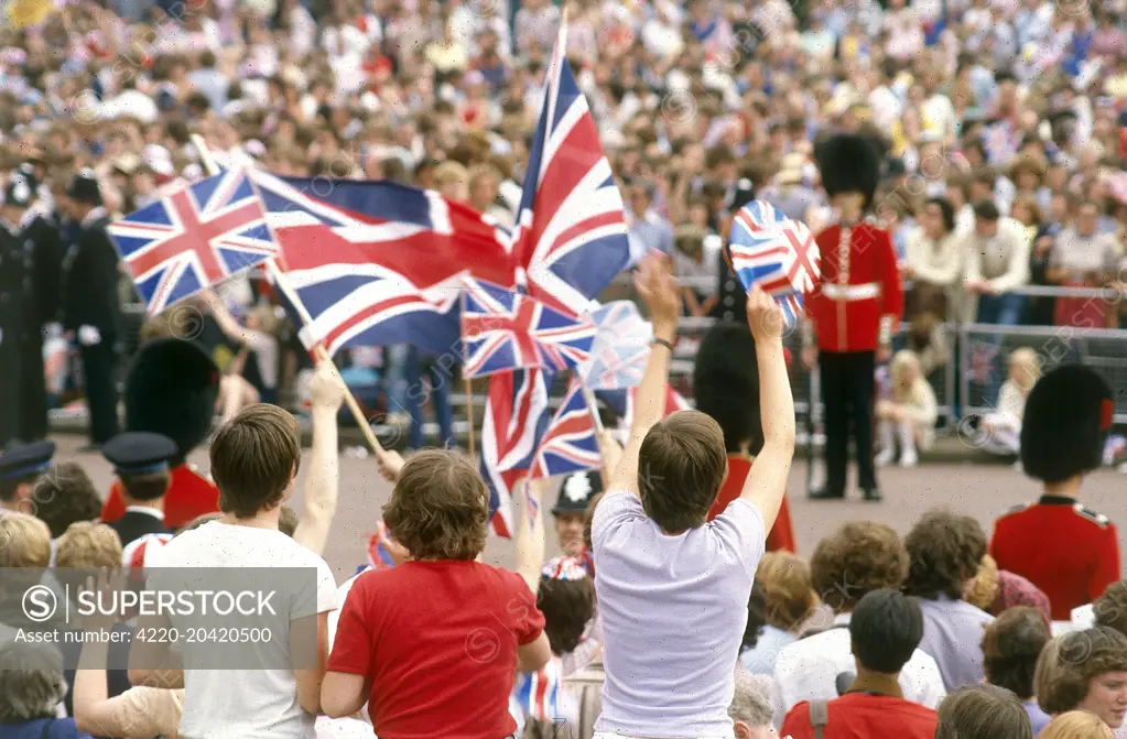 Crowds lining the processional route wave flags and cheer during the royal wedding between Prince Charles, Prince of Wales and Lady Diana Spencer at St Paul's Cathedral on 29 July 1981.     Date: 1981