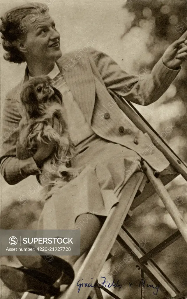 The English singer and actress, Gracie Fields (1898-1979), with her dog Ming, sitting at the top of a slide.       Date: 1938