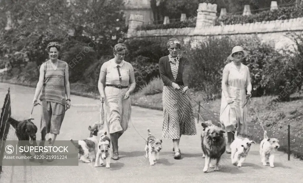 Four women with seven dogs on leads, Bournemouth.      Date: circa 1930s