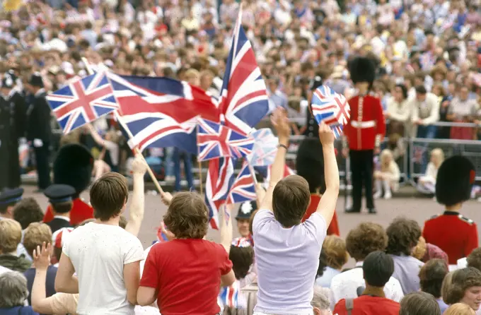 Crowds lining the processional route wave flags and cheer during the royal wedding between Prince Charles, Prince of Wales and Lady Diana Spencer at St Paul's Cathedral on 29 July 1981.     Date: 1981