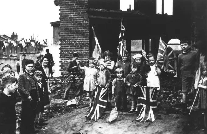 Children celebrate victory day in Europe by waving the union flag in a bombed out house in South London, May 8th 1945  1945