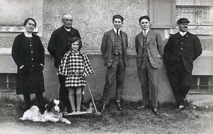 Six people (a woman, four men and a girl with a scooter) and a dog, France.      Date: circa 1920s