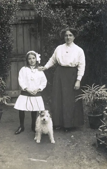 Woman and girl with a dog in a garden.      Date: circa 1910s