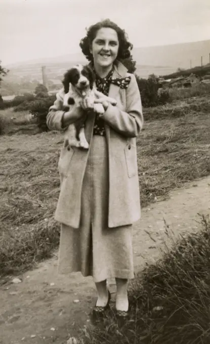 Woman holding a spaniel puppy on a hillside.      Date: circa 1930s