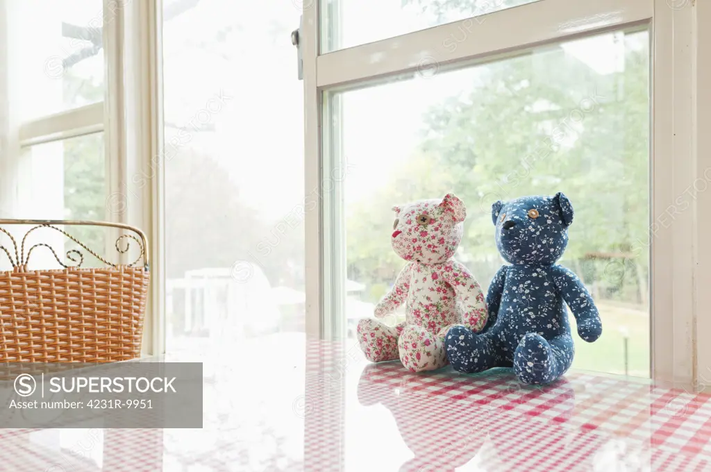 Two hand made children's soft toys sitting on a table. Teddy bears. Teddys. Window. Checked gingham table cloth.