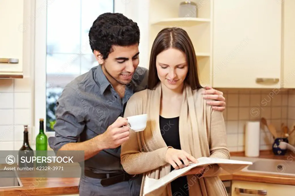 Young couple reading a newspaper together in the kitchen