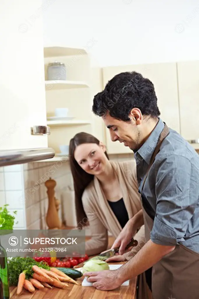 Man cutting kohlrabi in kitchen while woman is watching him