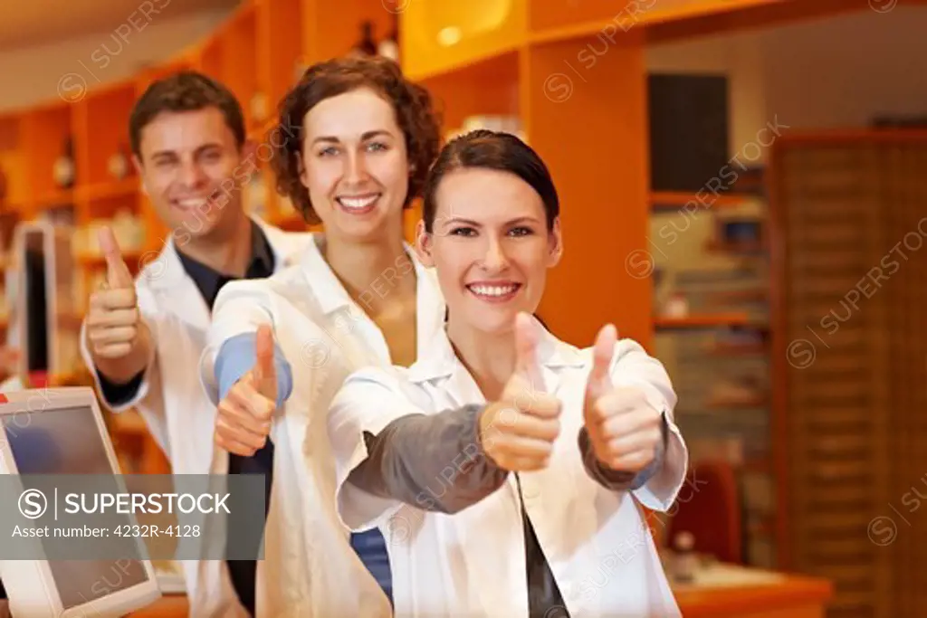 Three happy pharmacists holding their thumbs up in pharmacy
