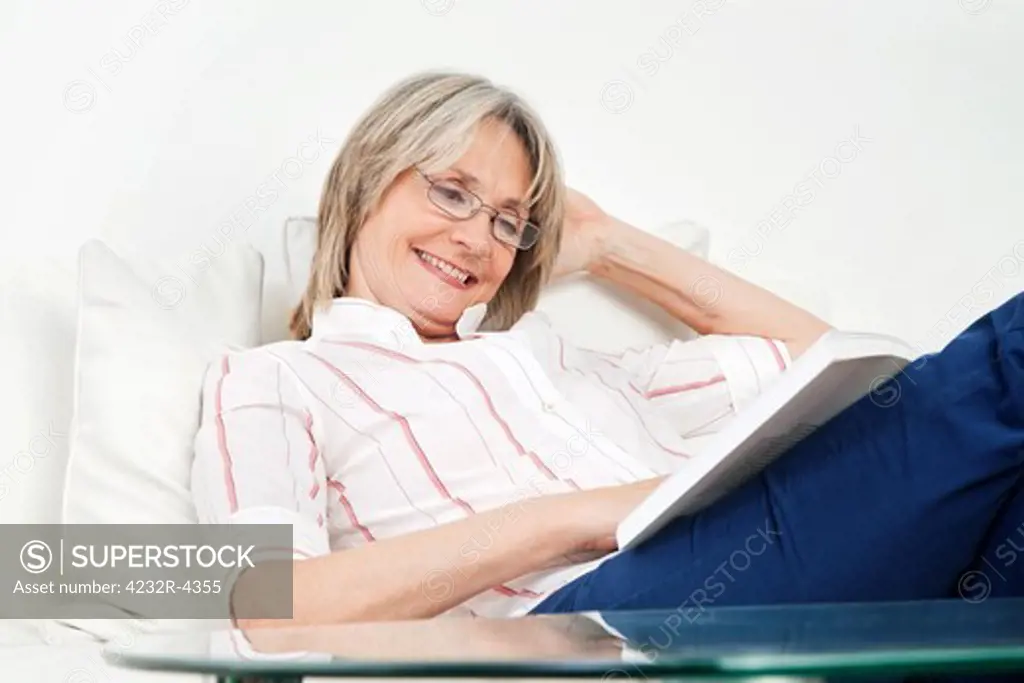 Happy senior woman reading a book on the couch