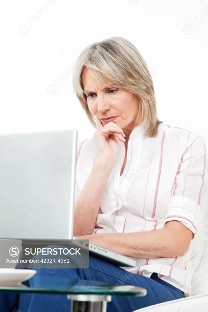 Frustrated senior woman with laptop at home on couch