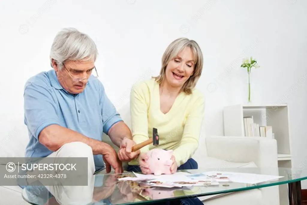 Senior couple breaking piggy bank with a hammer at home