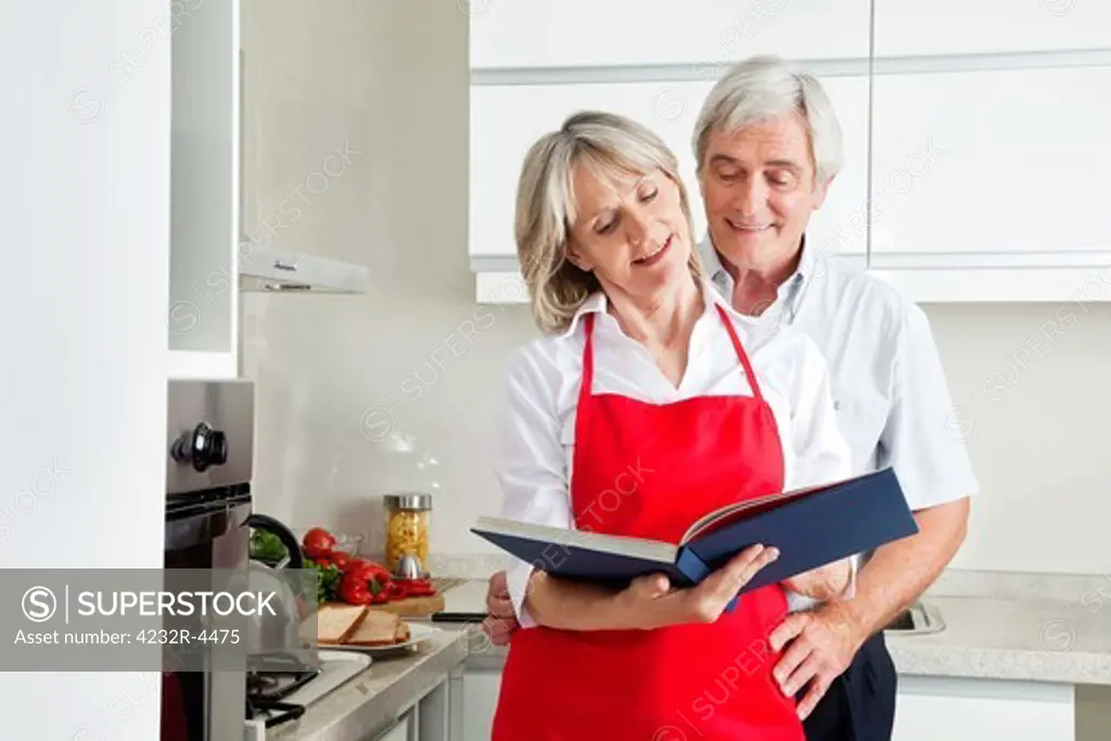 Happy senior couple in kitching looking for recipes in a cookbook