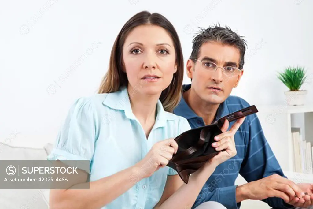 Elderly couple showing empty wallet in living room