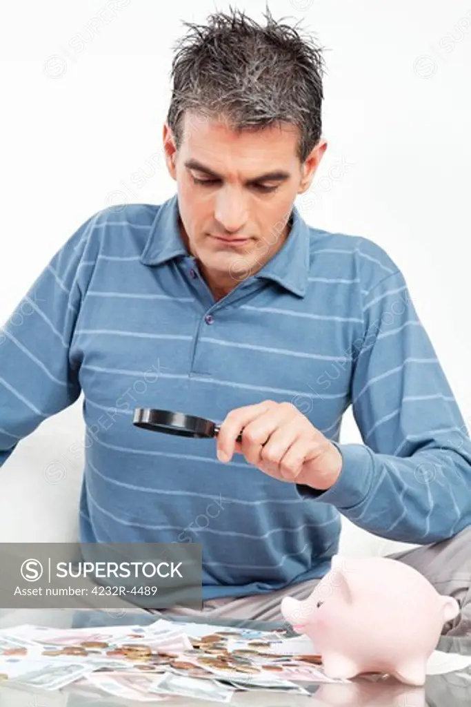Man with money and piggy bank looking through magnifying glass