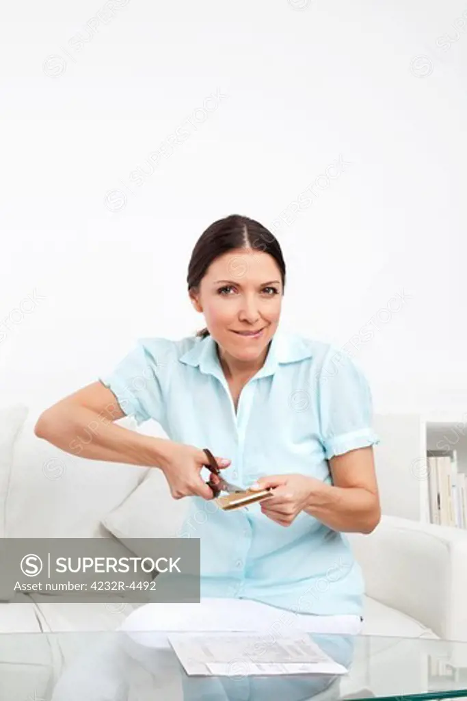 Elderly woman cutting credit card with scissors in living room