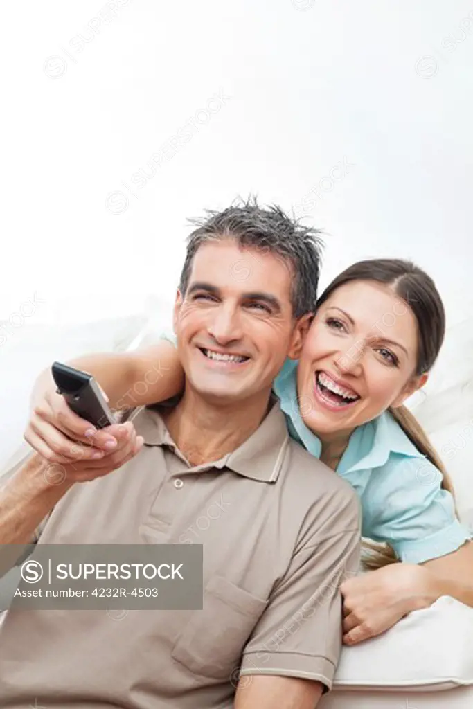 Happy couple watching TV with remote control at home