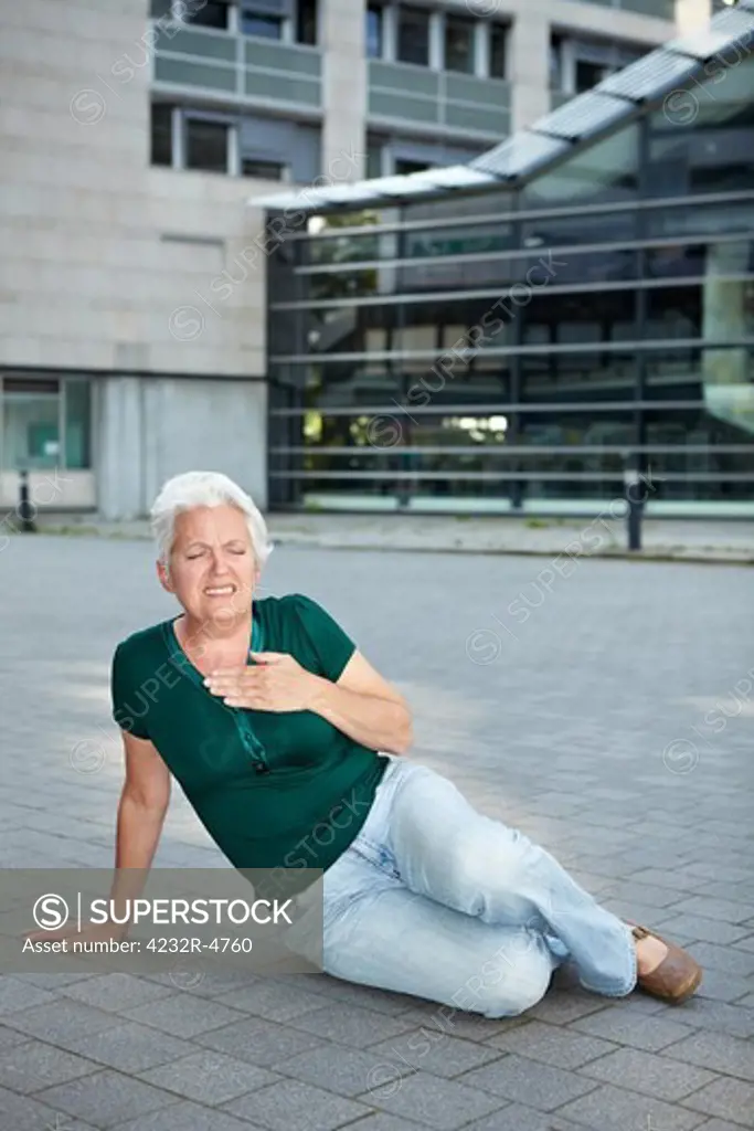 Senior woman with heart attack sitting on sidewalk