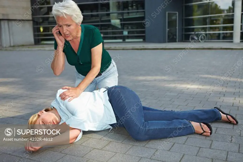 Senior woman with helpless woman calling ambulance with cell phone