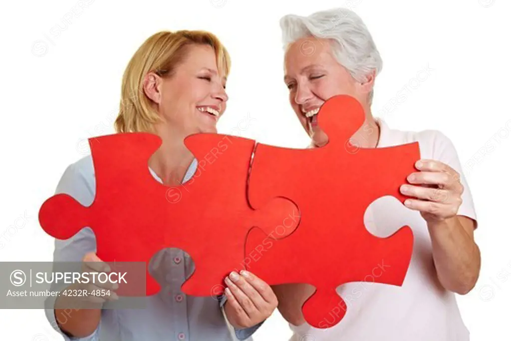 Two happy senior women holding jigsaw puzzle pieces