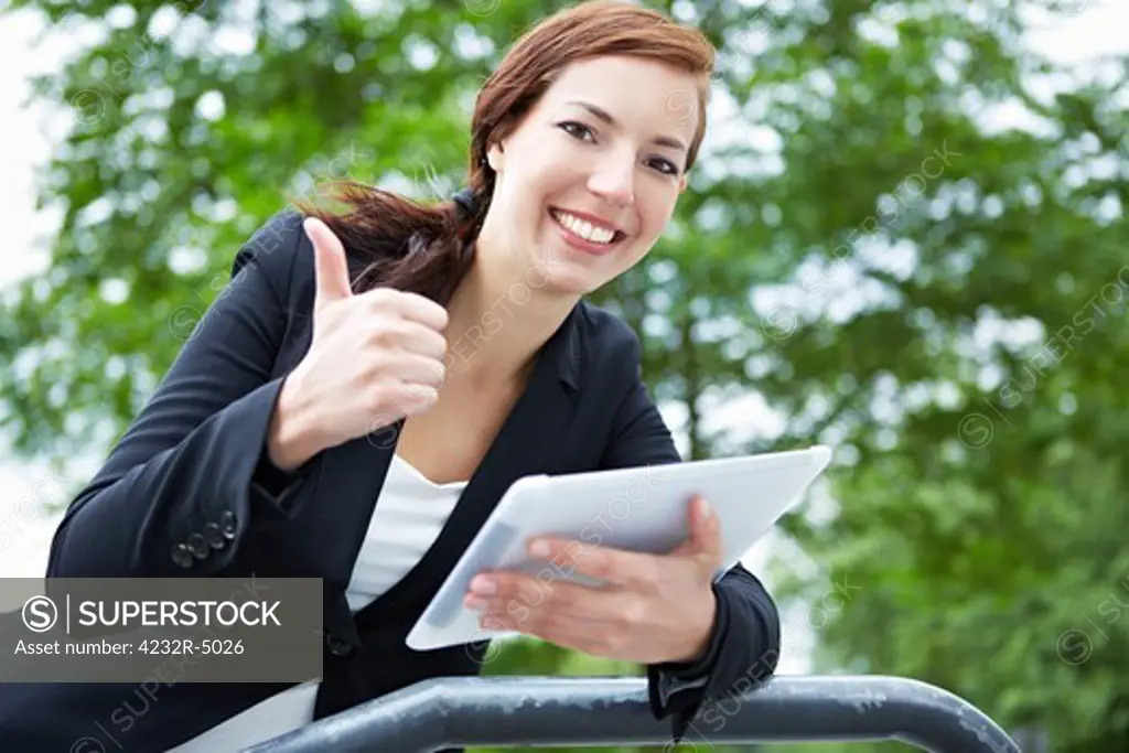 Happy business woman with tablet computer holding thumbs up