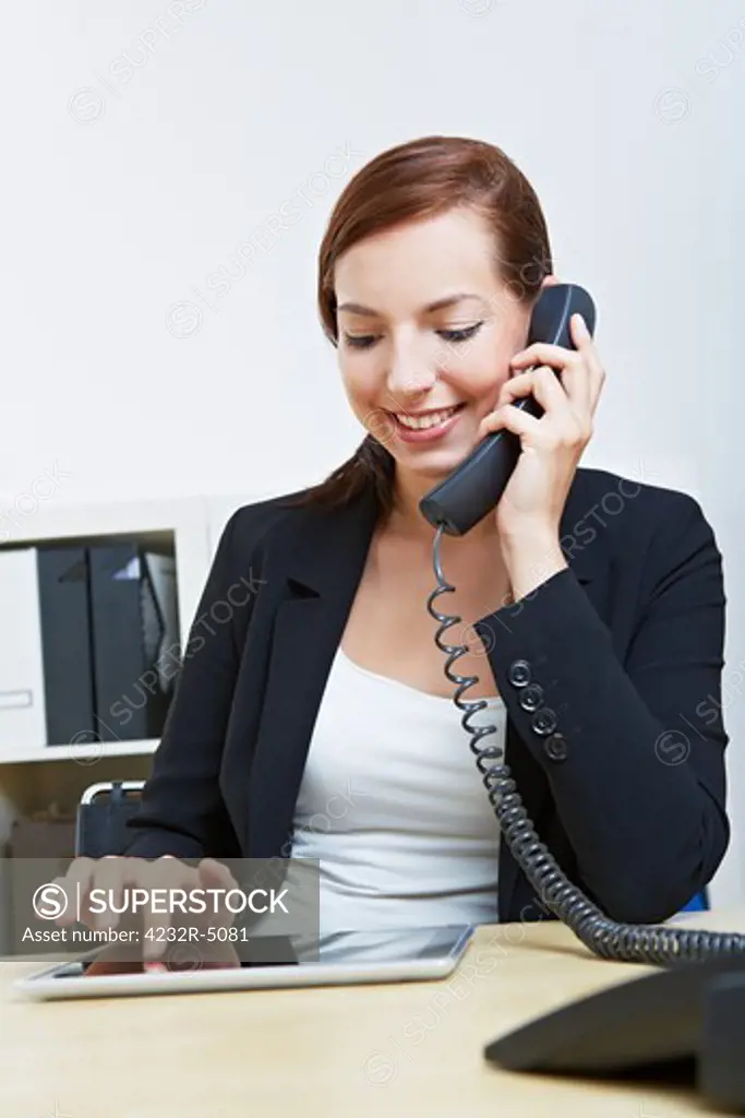 Business woman with tablet pc in her office making a phone call