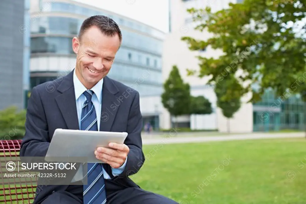 Happy business man using tablet PC outside on a park bench
