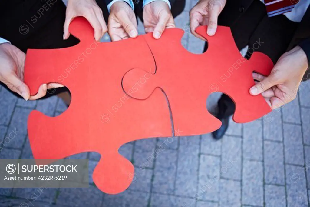 Many hands holding two red jigsaw puzzle pieces