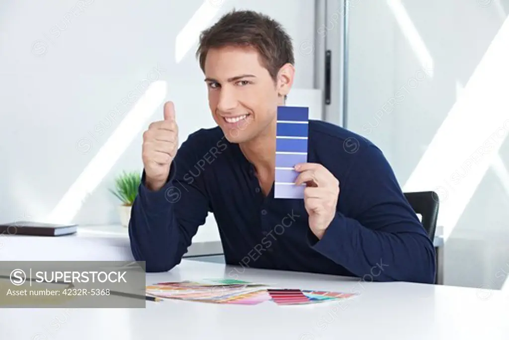 Designer with blue color samples at his desk in the office holding thumbs up