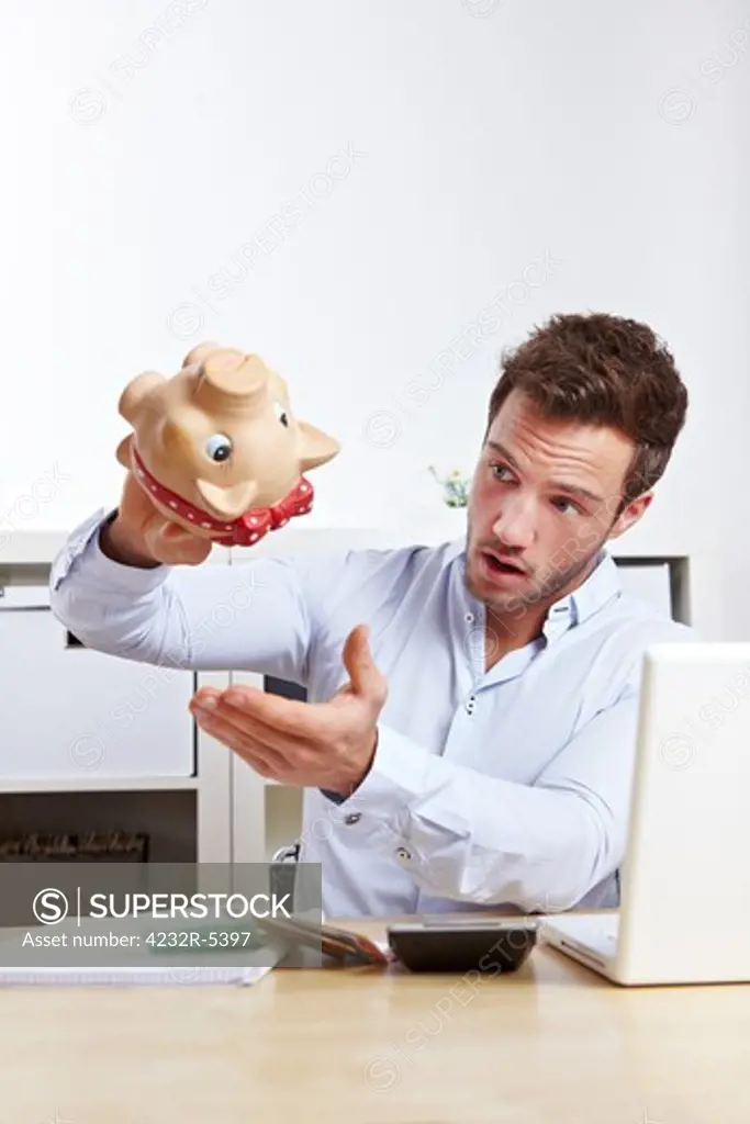 Shocked university student shaking empty piggy bank at desk