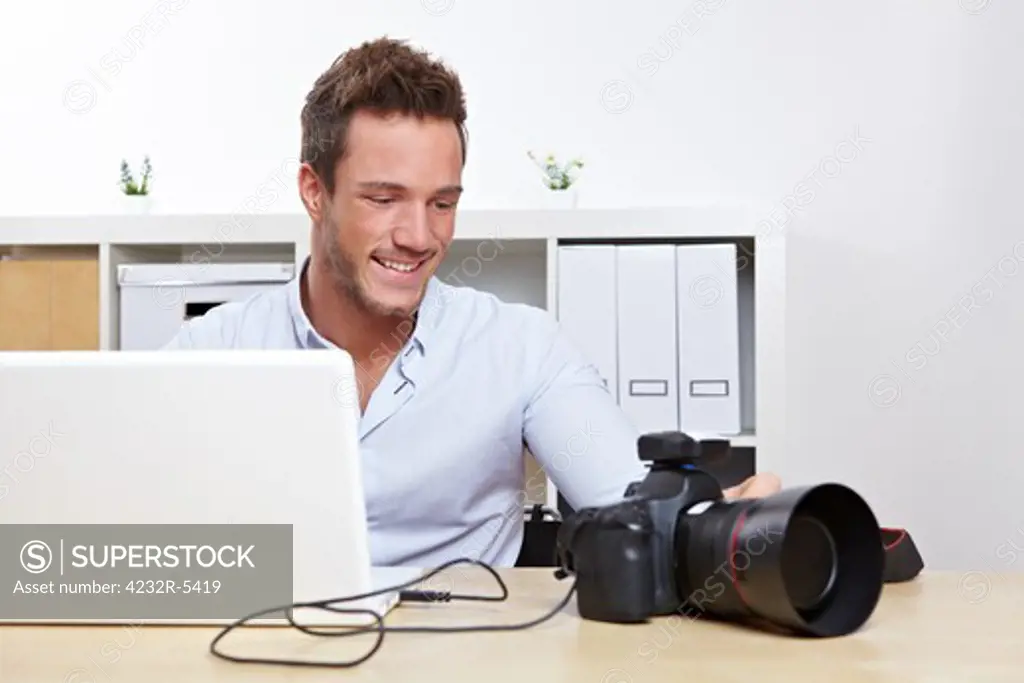 Happy photographer downloading photos from camera to laptop computer