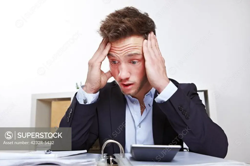 Shocked young business man in office looking at files