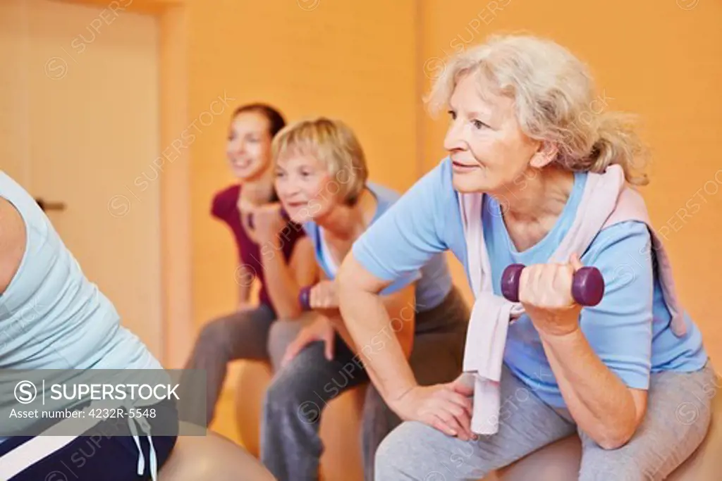 Smiling senior woman in a group doing back training exercises with dumbbells