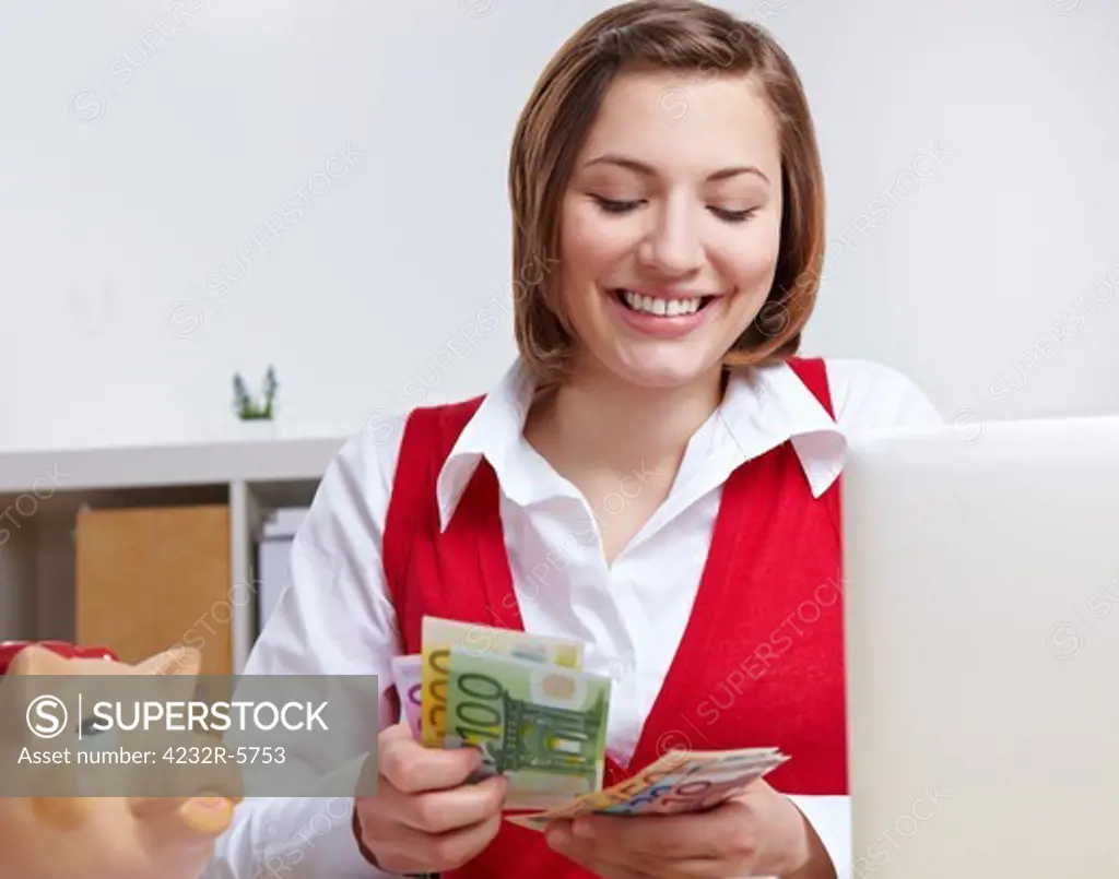 Happy business woman in office counting Euro money at her desk