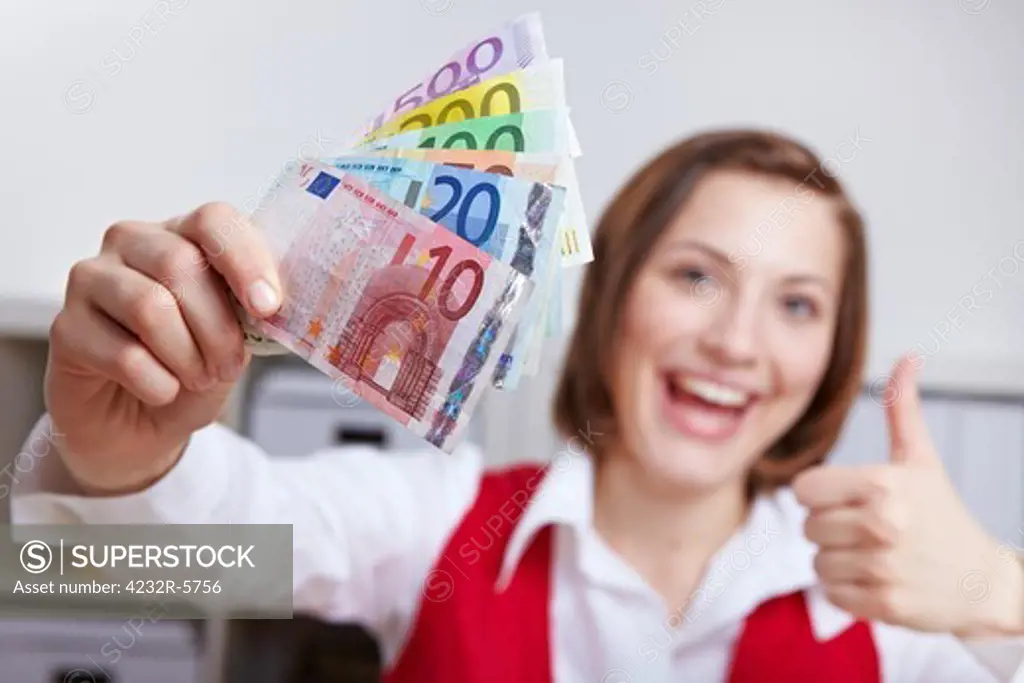 Happy woman in office with Euro money fan holding her thumbs up
