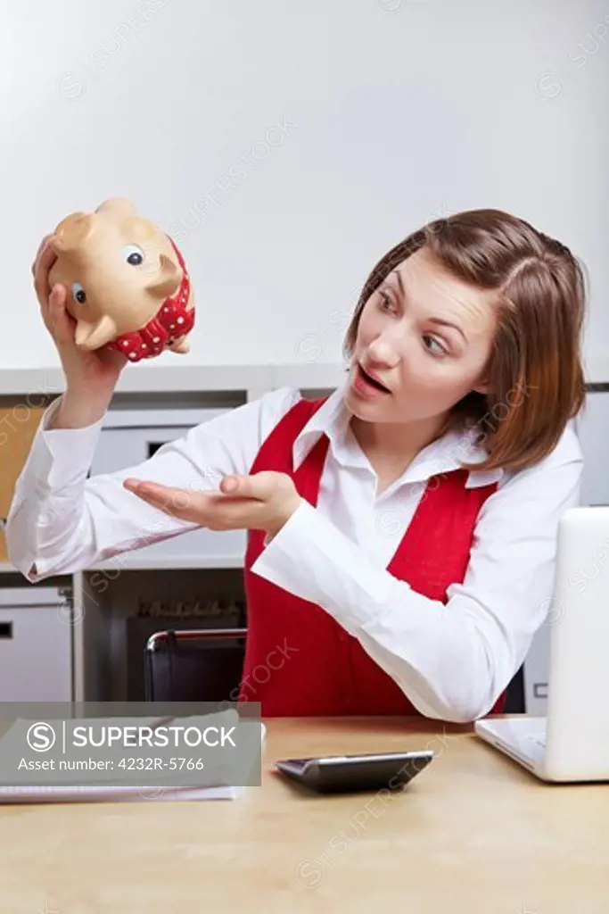 Shocked woman shaking an empty piggy bank in business office