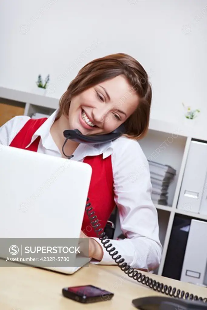 Smiling female student at desk with laptop computer using phone