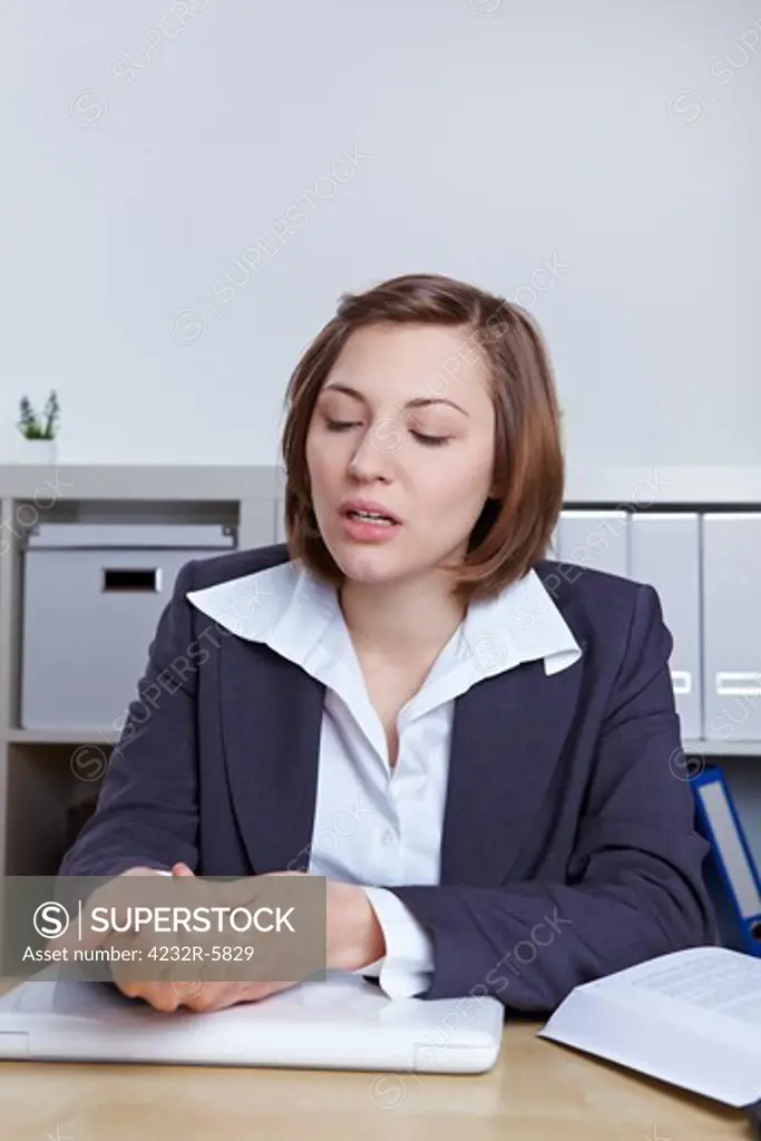 Business woman sitting with wrist pain at her desk in the office