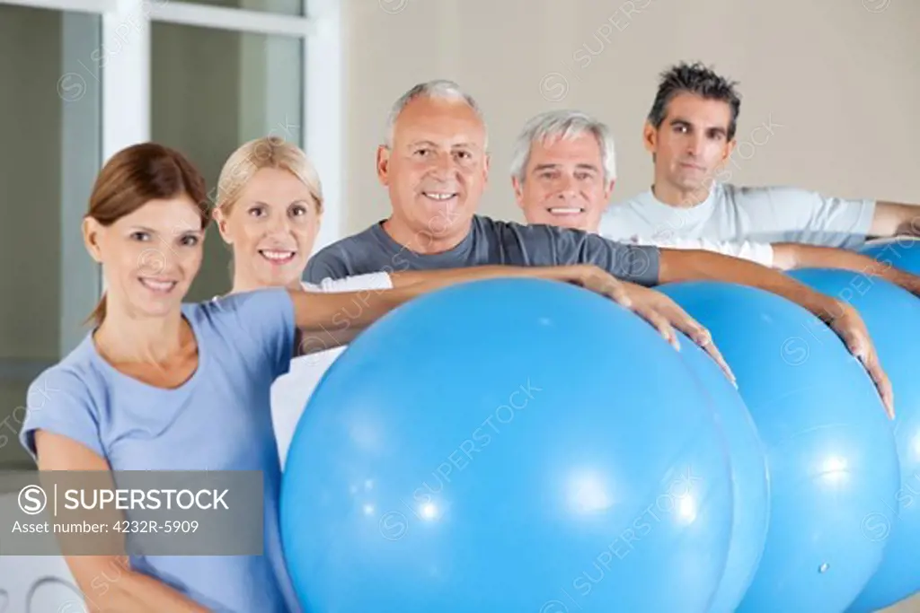 Happy senior citizens holding blue gym balls in fitness center