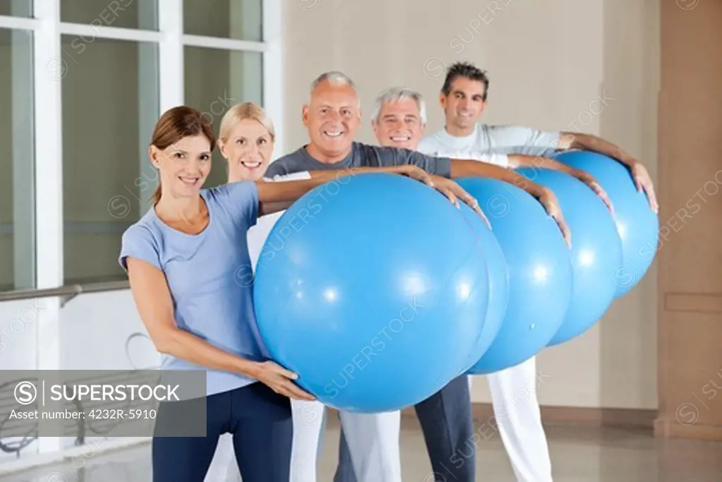 Senior group carrying blue gym balls in fitness center
