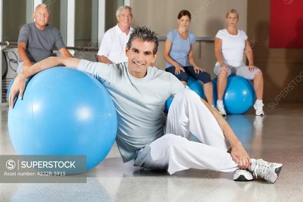 Happy man sitting with blue gym ball in fitness center with senior group