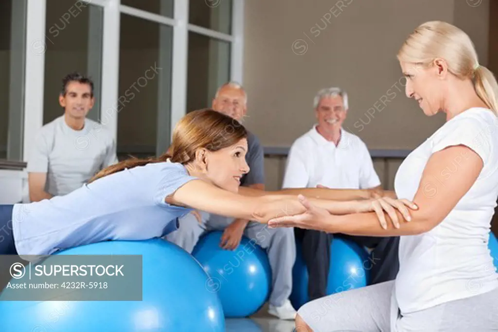 Fitness trainer helping woman doing back exercises in gym
